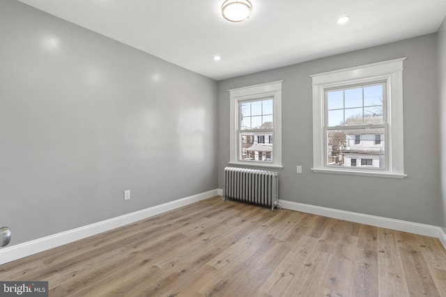 empty room with recessed lighting, radiator, light wood-type flooring, and baseboards