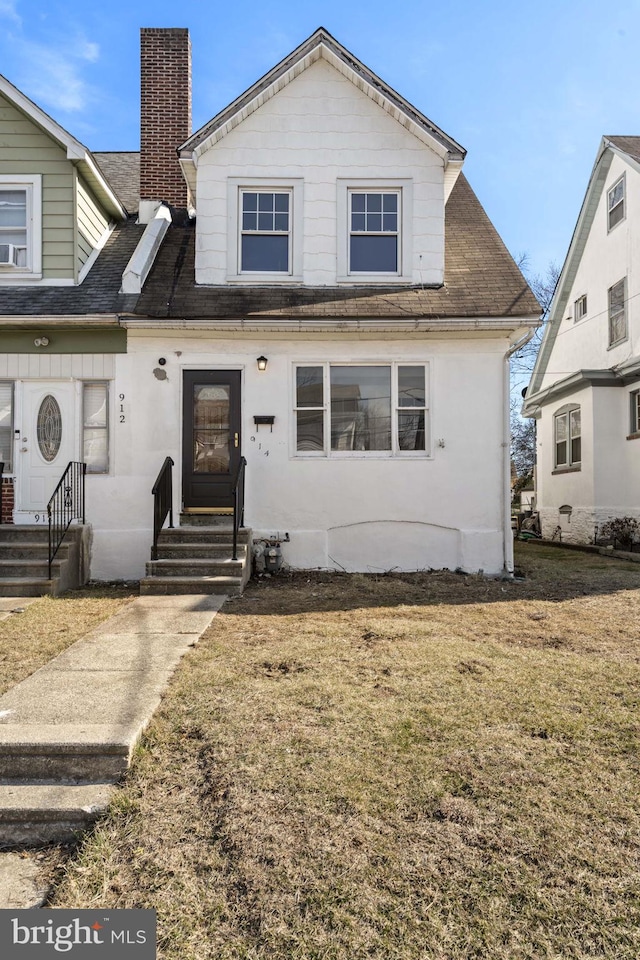 view of front facade with entry steps, a chimney, and a front lawn