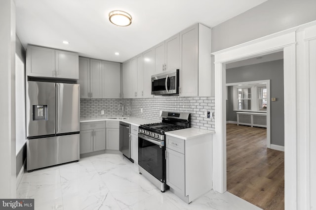 kitchen featuring tasteful backsplash, gray cabinets, marble finish floor, stainless steel appliances, and a sink