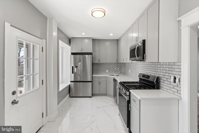 kitchen featuring backsplash, light countertops, gray cabinets, appliances with stainless steel finishes, and marble finish floor