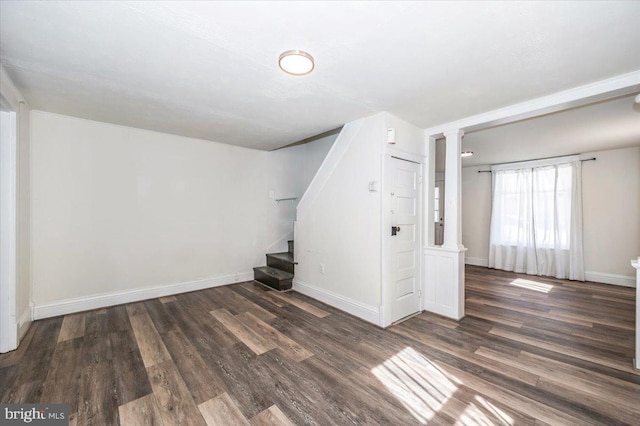 unfurnished room featuring stairway, baseboards, wood finished floors, and ornate columns