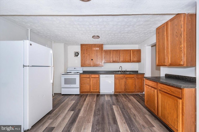 kitchen featuring white appliances, dark wood finished floors, a sink, dark countertops, and brown cabinets