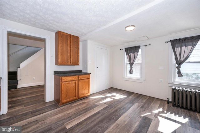 kitchen featuring brown cabinetry, a textured ceiling, radiator heating unit, and dark wood-style flooring