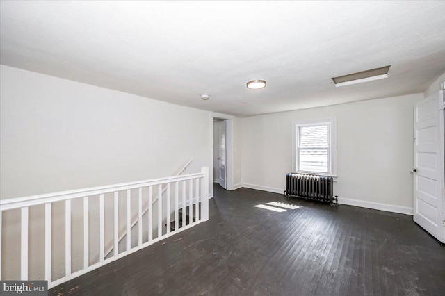 empty room featuring radiator, wood finished floors, and baseboards