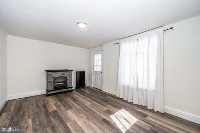 unfurnished living room with a fireplace, radiator heating unit, baseboards, and wood finished floors