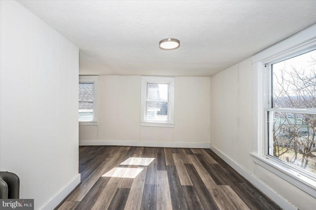 unfurnished room with baseboards, dark wood-style flooring, and a textured ceiling