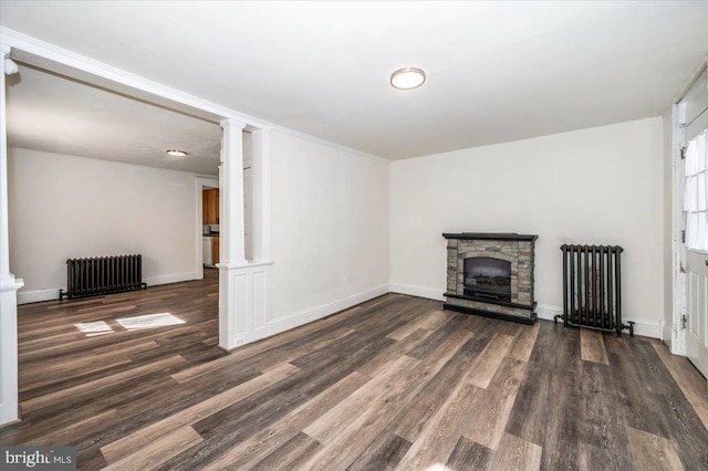 unfurnished living room with wood finished floors, radiator heating unit, a fireplace, and decorative columns