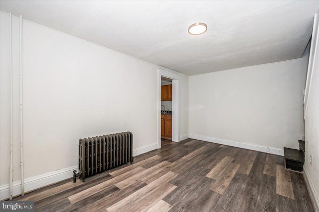 empty room featuring radiator, wood finished floors, baseboards, and a sink