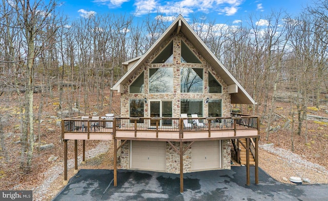 rear view of house featuring a garage, stone siding, and a wooden deck