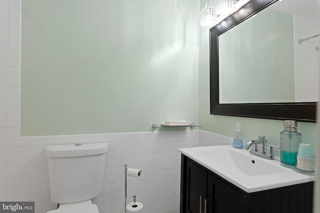bathroom with tile walls, a wainscoted wall, vanity, and toilet