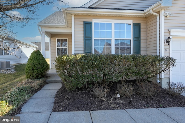 entrance to property with central AC unit and a shingled roof