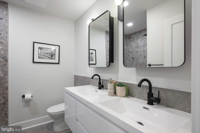 bathroom featuring double vanity, toilet, baseboards, and a sink