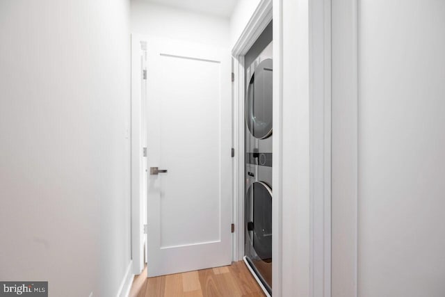 laundry area with laundry area, light wood-style flooring, and stacked washer and clothes dryer