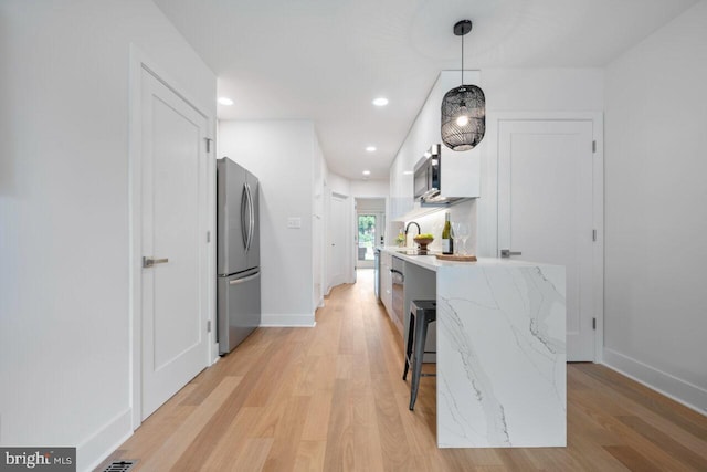 kitchen featuring light wood-style flooring, white cabinets, stainless steel appliances, and pendant lighting