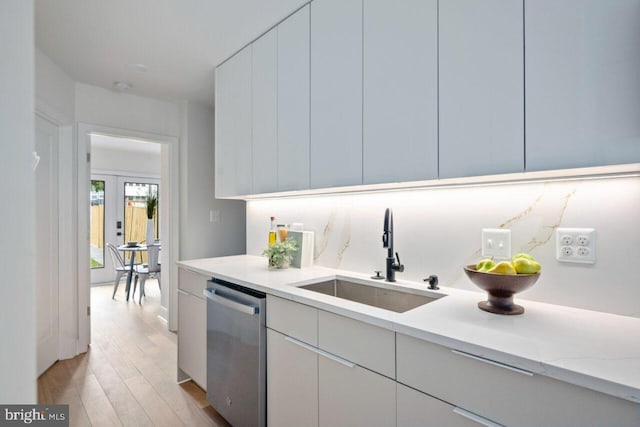 kitchen with light stone countertops, a sink, white cabinets, dishwasher, and light wood-type flooring