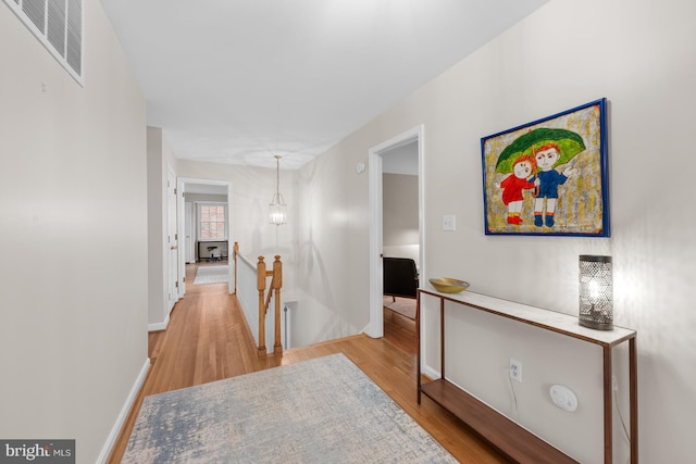 hallway with visible vents, an upstairs landing, a notable chandelier, light wood-style flooring, and baseboards