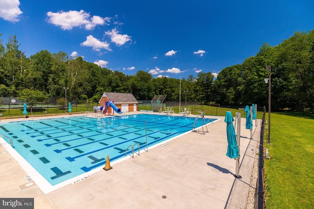 community pool featuring an outbuilding, fence, a water slide, a patio area, and a lawn