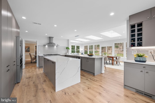 kitchen featuring visible vents, gray cabinetry, wall chimney exhaust hood, and a center island