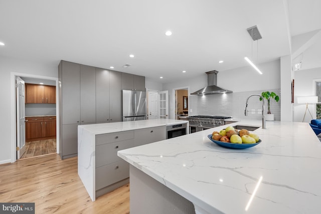 kitchen with a center island, wall chimney range hood, gray cabinetry, and stainless steel appliances