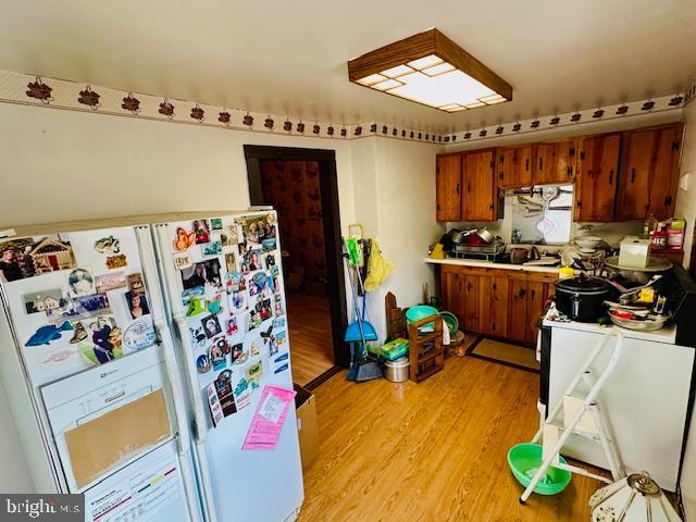 kitchen with brown cabinetry, light countertops, light wood-style floors, and white fridge with ice dispenser