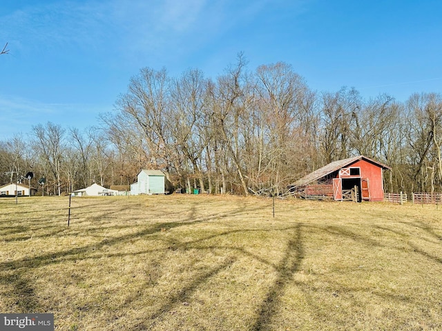 view of yard with a rural view, an outbuilding, a barn, and fence