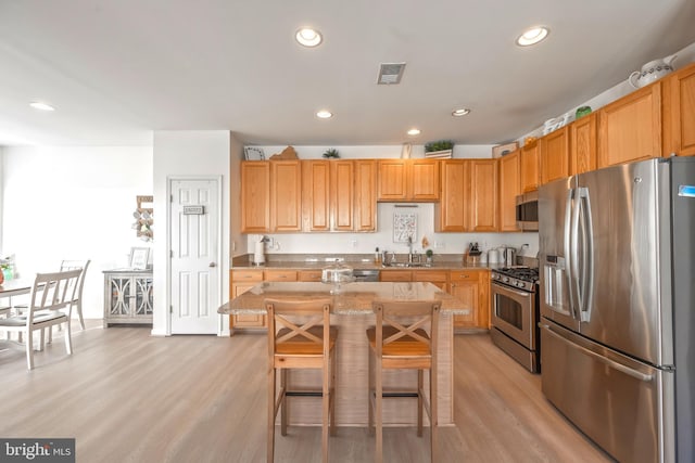 kitchen featuring a center island, light wood-type flooring, light stone counters, appliances with stainless steel finishes, and a sink