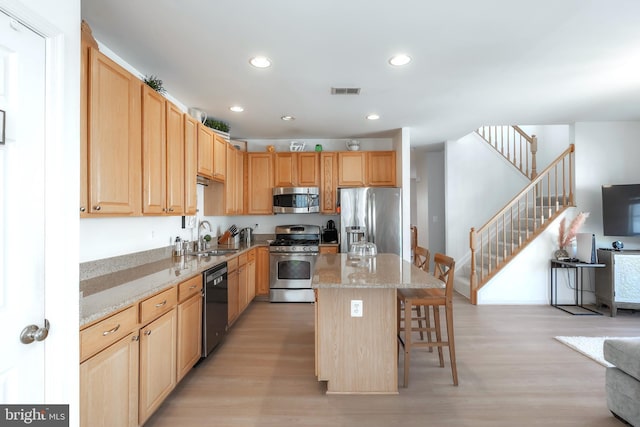 kitchen with light brown cabinetry, a center island, stainless steel appliances, and a sink