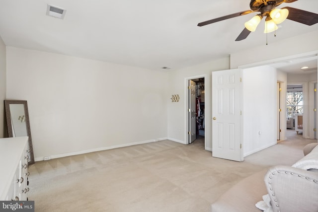 bedroom with visible vents, baseboards, ceiling fan, a walk in closet, and light colored carpet