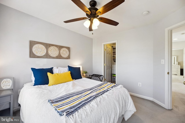 bedroom featuring light carpet, a ceiling fan, a walk in closet, and baseboards