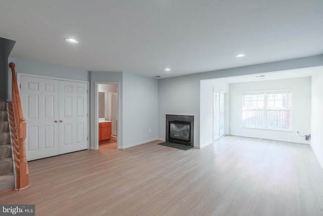 unfurnished living room featuring baseboards, light wood finished floors, a fireplace with flush hearth, recessed lighting, and stairs