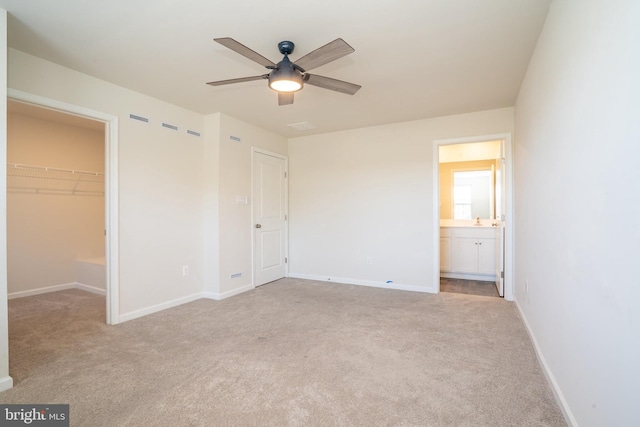 unfurnished bedroom with a closet, carpet flooring, baseboards, ceiling fan, and a spacious closet