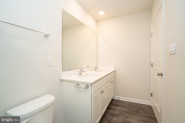 bathroom with toilet, a sink, wood finished floors, double vanity, and baseboards