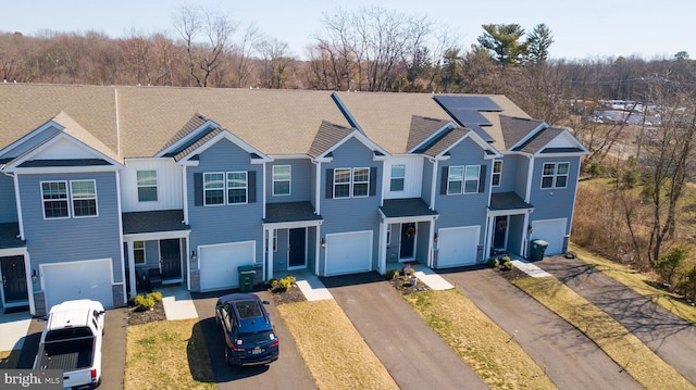 view of front facade with roof mounted solar panels, an attached garage, a shingled roof, and driveway