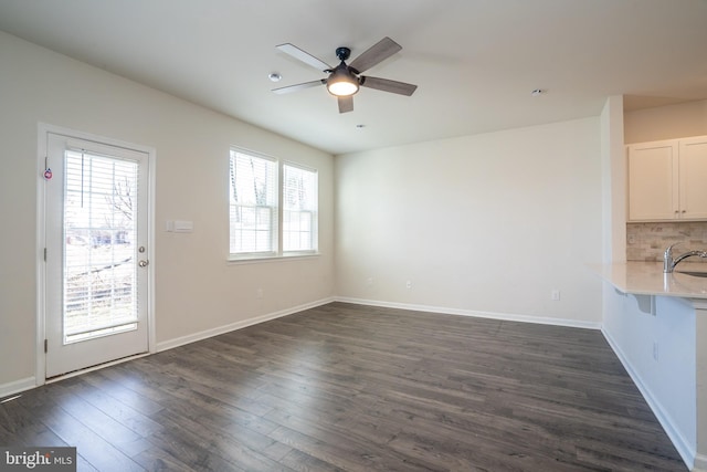 unfurnished living room with a sink, baseboards, dark wood-type flooring, and ceiling fan