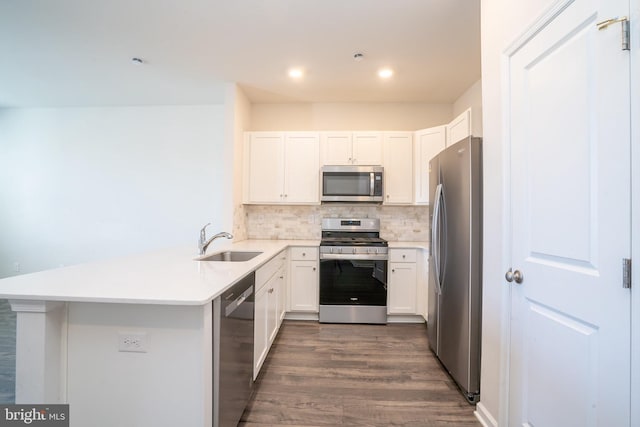 kitchen with a sink, tasteful backsplash, dark wood finished floors, appliances with stainless steel finishes, and a peninsula