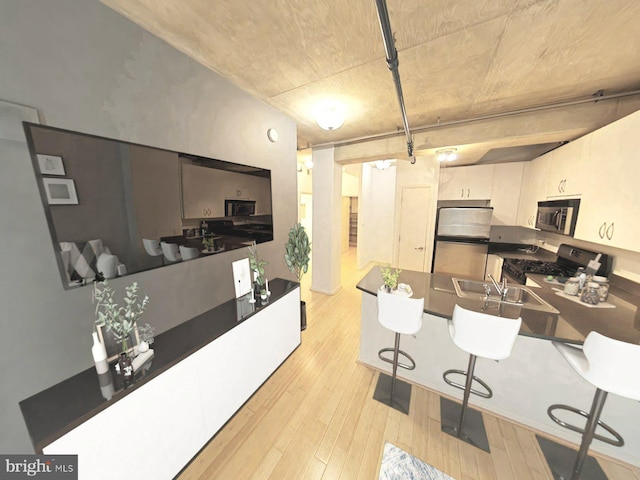 kitchen featuring a peninsula, light wood-style flooring, a sink, stainless steel appliances, and white cabinetry