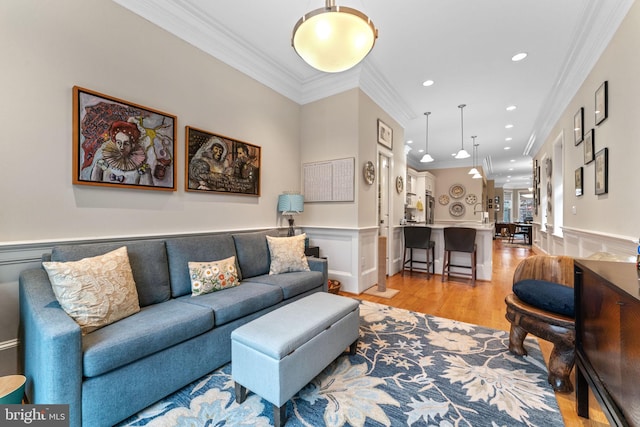 living area featuring crown molding, light wood-style flooring, and a wainscoted wall