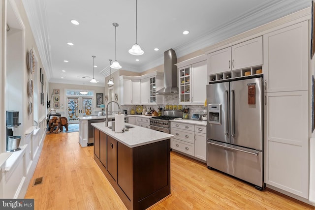 kitchen featuring visible vents, wall chimney range hood, an island with sink, premium appliances, and a sink