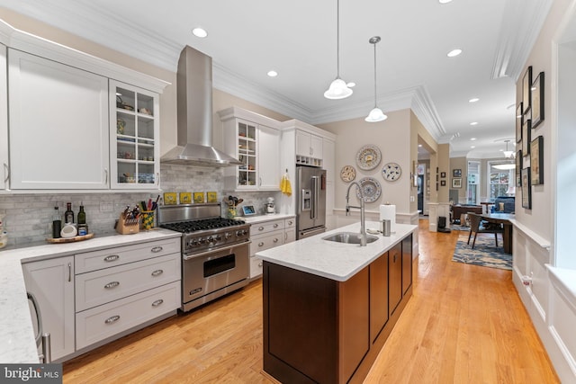 kitchen with light wood-style flooring, high quality appliances, wall chimney exhaust hood, and a sink