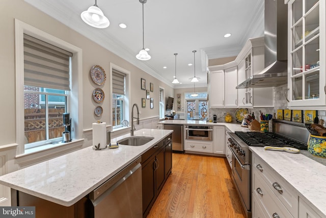 kitchen featuring a peninsula, a sink, ornamental molding, stainless steel appliances, and wall chimney range hood