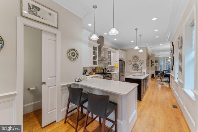 kitchen with visible vents, a center island with sink, a sink, premium appliances, and wall chimney range hood