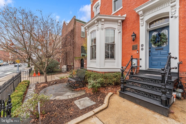 doorway to property featuring fence and brick siding