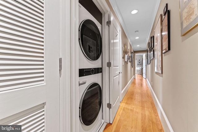 clothes washing area featuring light wood-type flooring, stacked washing maching and dryer, recessed lighting, baseboards, and laundry area