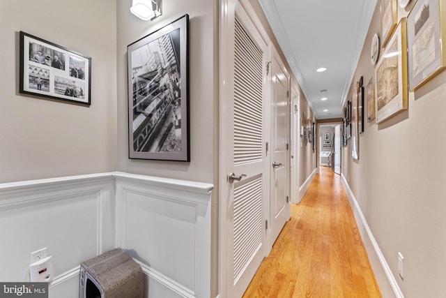 hallway featuring crown molding, recessed lighting, wainscoting, light wood-style floors, and a decorative wall