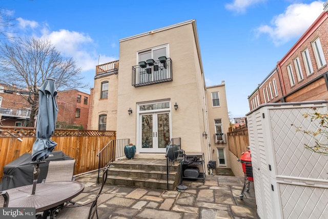 back of property with stucco siding, fence, french doors, a balcony, and a patio area