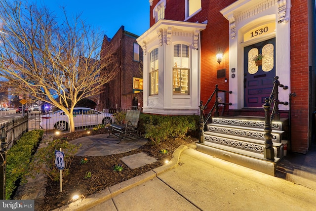 view of exterior entry featuring fence and brick siding