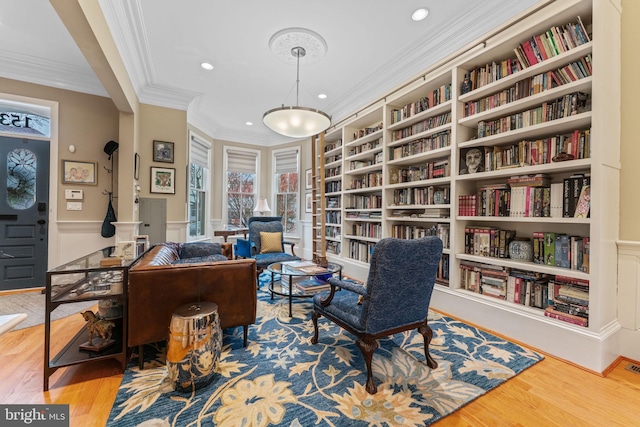 home office featuring wainscoting, wood finished floors, wall of books, and ornamental molding