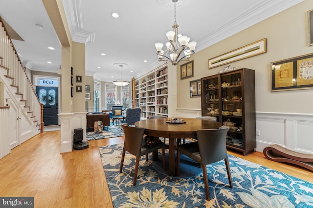 dining area with built in shelves, light wood-style flooring, stairway, wainscoting, and crown molding