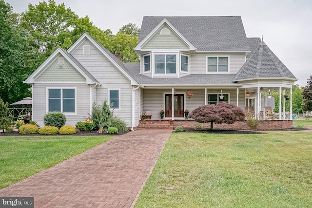 victorian-style house featuring a porch, a front yard, and roof with shingles