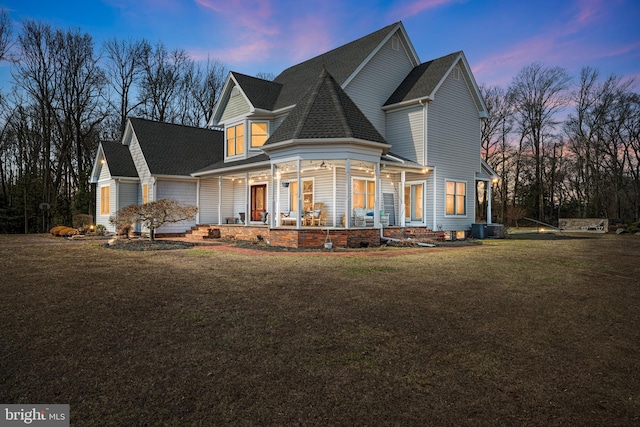 view of front of house featuring cooling unit, a porch, a shingled roof, and a front yard